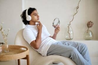 A mixed-race man applies face toner while listening to music on headphones.