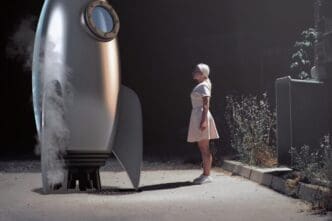 Woman stands beside a rocket, viewed from the side.