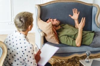 Side view of a young, white man on a couch gestures with his hands while talking during a therapy session.