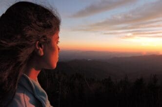 Side profile of a young woman gazing at a vibrant sunset.