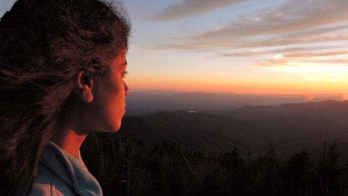 Side profile of a young woman gazing at a vibrant sunset.
