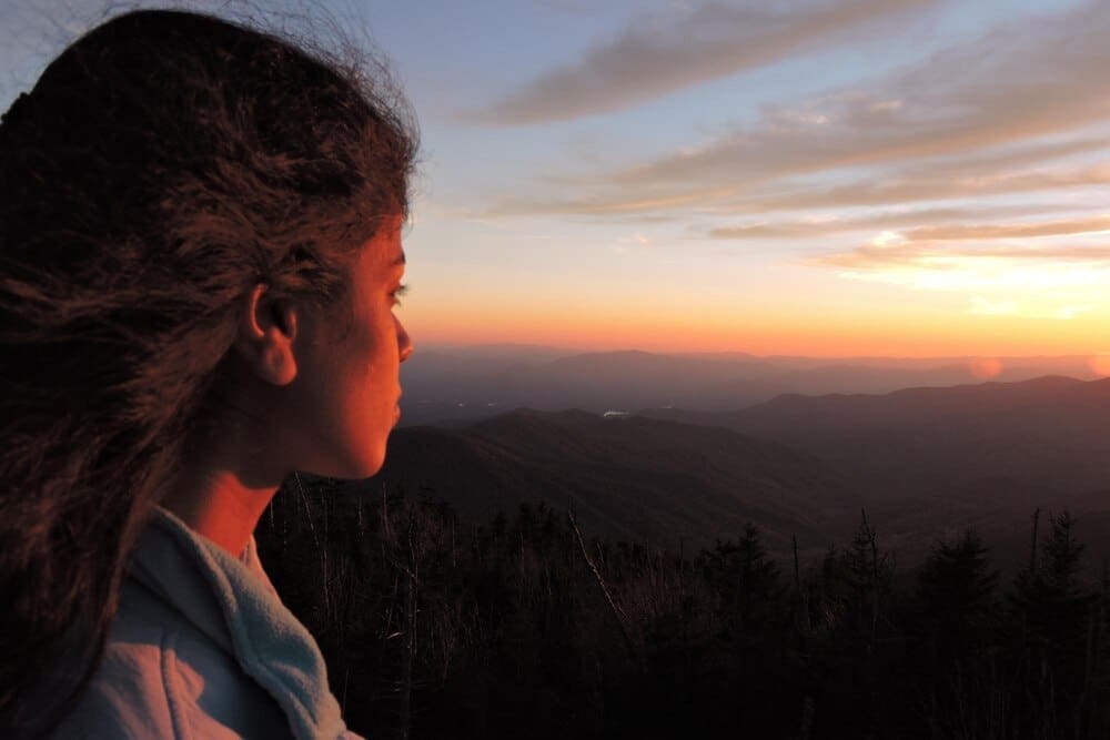Side profile of a young woman gazing at a vibrant sunset.