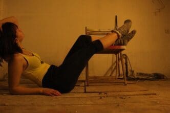 A young woman reclines on a hardwood floor, viewed from the side.