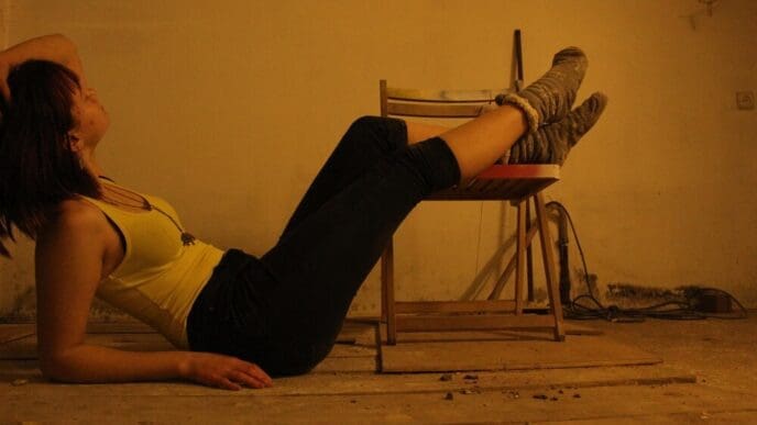A young woman reclines on a hardwood floor, viewed from the side.