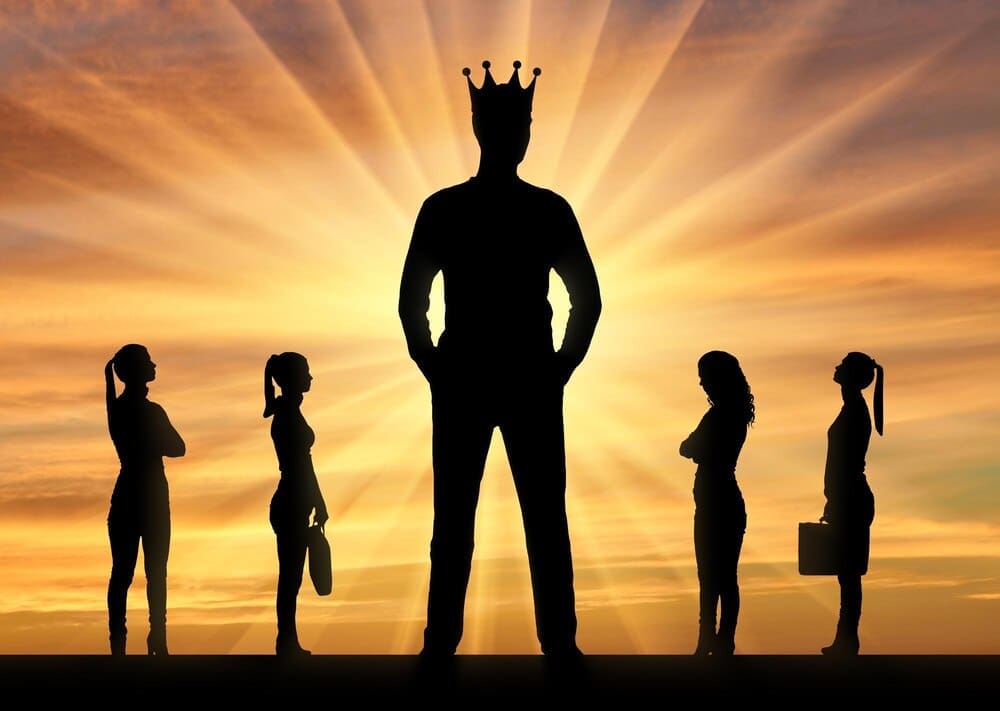 Silhouette of a large man wearing a crown stands prominently, with four smaller women positioned near him, representing gender inequality.