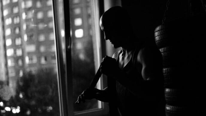 Silhouette of a muscular boxer wrapping tape around their arms in a dark gym, preparing for a fight.