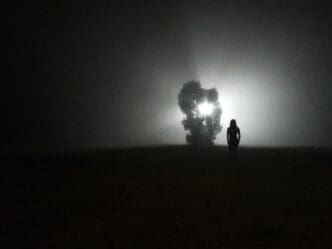 Silhouette of a woman standing outdoors at night against a starry sky.
