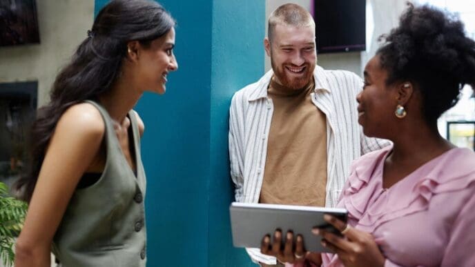 A man smiles while speaking to a manager and colleague during a business meeting in an office.
