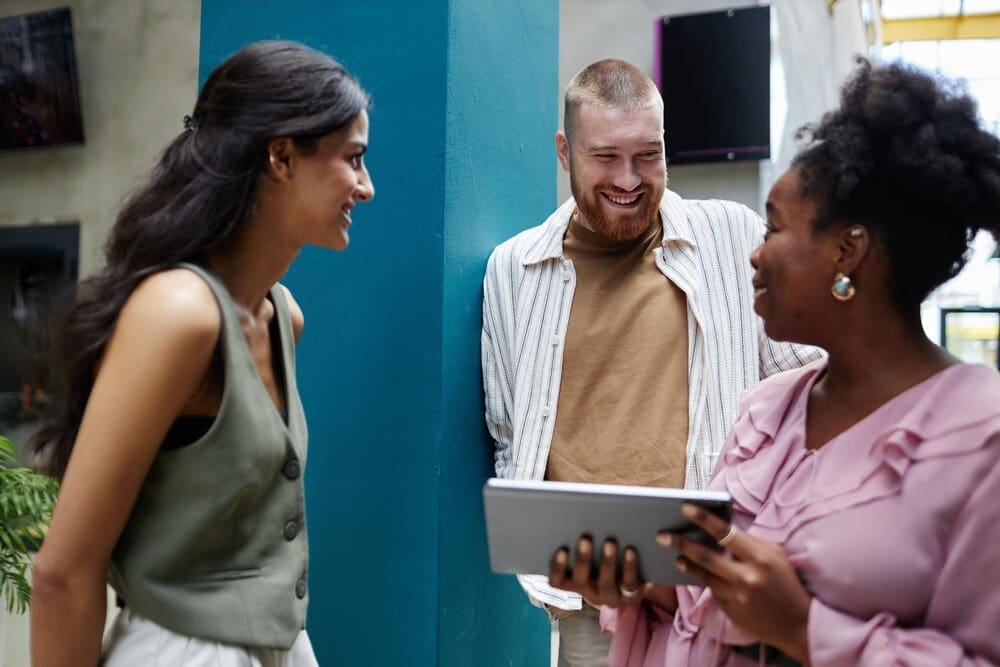 A man smiles while speaking to a manager and colleague during a business meeting in an office.