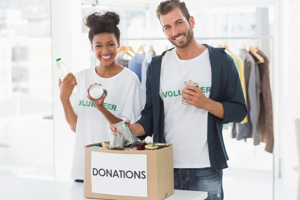 A young couple smiles while holding a donation box.