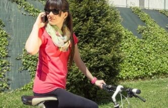 A woman in athletic wear uses a phone while standing next to a fixed-gear bicycle.