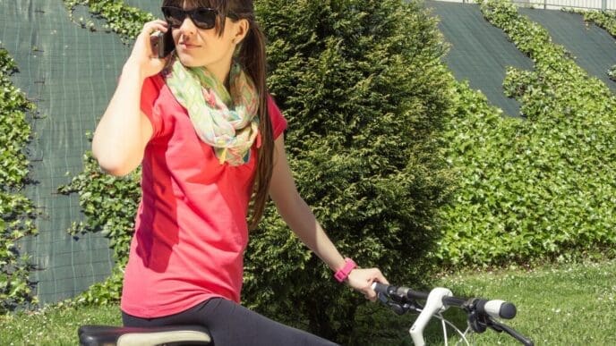 A woman in athletic wear uses a phone while standing next to a fixed-gear bicycle.