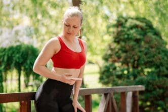Blond woman in athletic wear rests in a park, using her phone with earphones after a workout.
