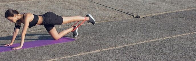 A slender girl in workout clothes stands near a concrete wall with a training mat on the ground.