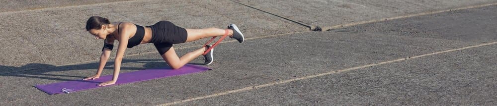 A slender girl in workout clothes stands near a concrete wall with a training mat on the ground.