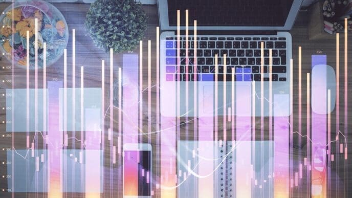 A multi-exposure image shows a stock market graph overlaid on a top-down view of a computer on a table, representing financial education.