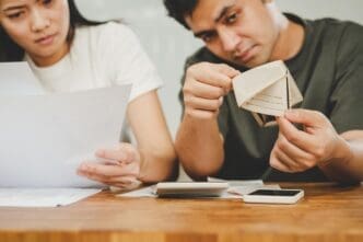 An Asian couple looks stressed while reviewing finances, indicating financial strain and possible debt.