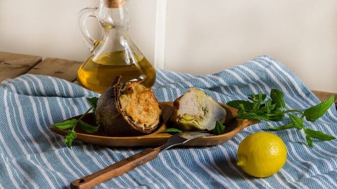Stuffed artichokes, garnished with fresh mint, are served on a plate, showcasing a Mediterranean dish with mushrooms, onion, minced meat, and cheese.