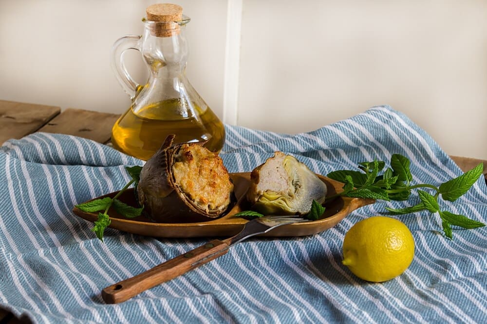 Stuffed artichokes, garnished with fresh mint, are served on a plate, showcasing a Mediterranean dish with mushrooms, onion, minced meat, and cheese.