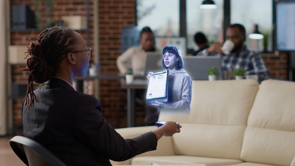 A businesswoman in a high-tech office participates in a holographic teleconference with a team leader and an African American worker.