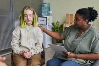 A teenage girl sits in a chair, talking with a specialist who is giving her advice during a therapy session.