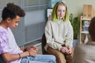 A teenage girl sits in a chair and speaks in a group therapy session.