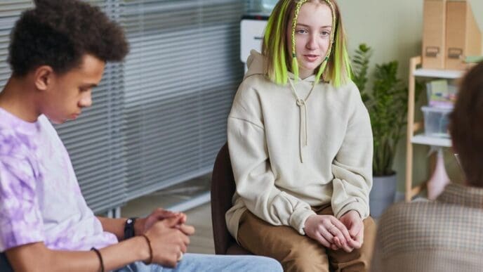 A teenage girl sits in a chair and speaks in a group therapy session.