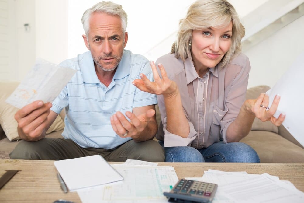 A mature couple looks concerned while reviewing bills with a calculator.