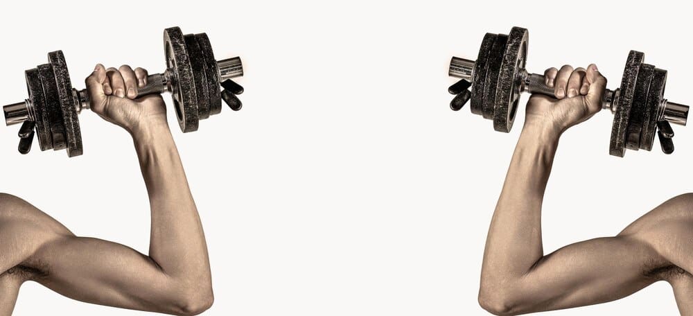 A thin man in athletic wear lifts a dumbbell, showcasing his bicep muscle.