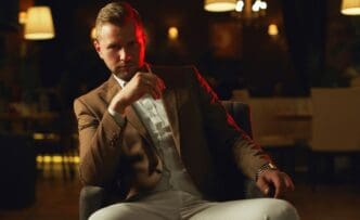A well-dressed man in a suit poses thoughtfully in a restaurant.