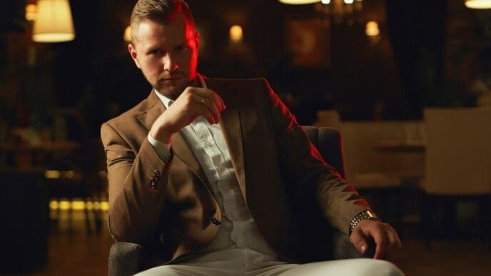 A well-dressed man in a suit poses thoughtfully in a restaurant.