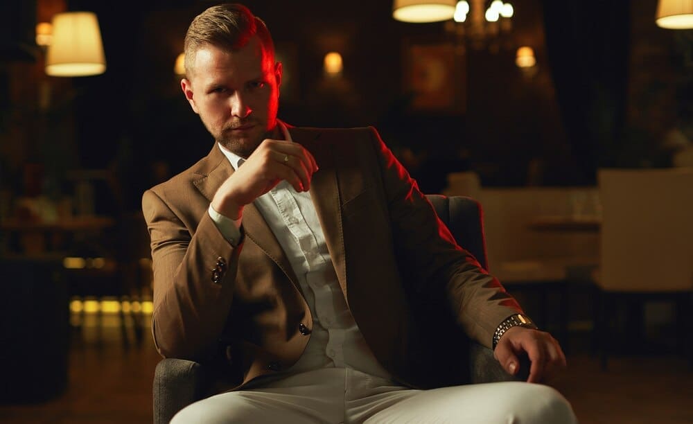 A well-dressed man in a suit poses thoughtfully in a restaurant.
