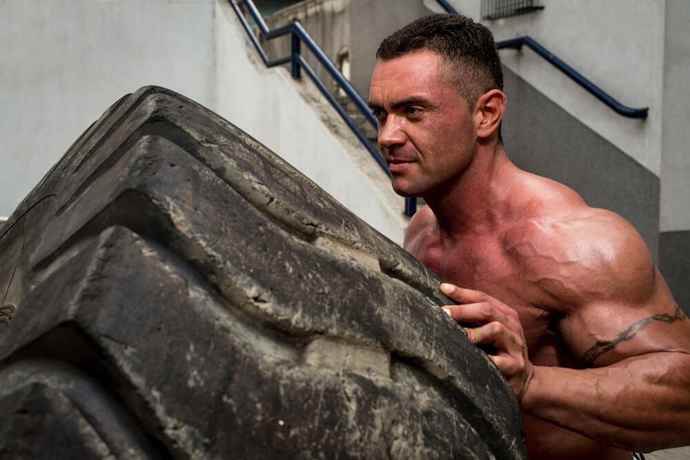 A person performs a workout by flipping a large tire.