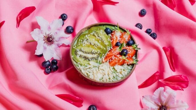 Top-down view of colorful fruit dishes in bowls arranged on a pink cloth.