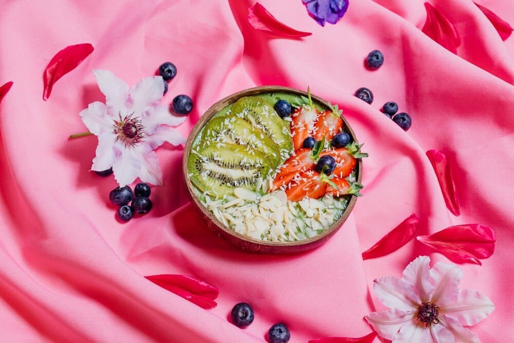 Top-down view of colorful fruit dishes in bowls arranged on a pink cloth.