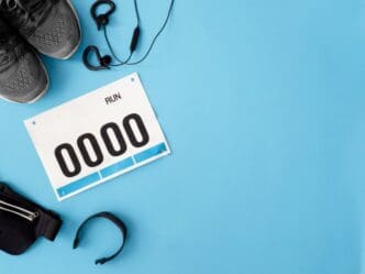 Top-down view of running shoes, a bib number, and running accessories arranged on a blue background, representing a running event.