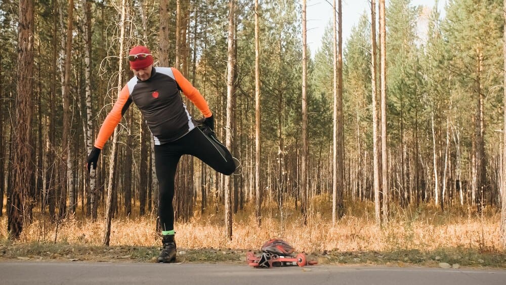 An adult man in a helmet and athletic gear uses ski poles while roller skiing on a paved road.