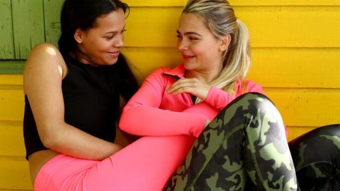 Two young, smiling women of the same race embrace, likely a couple, expressing affection.