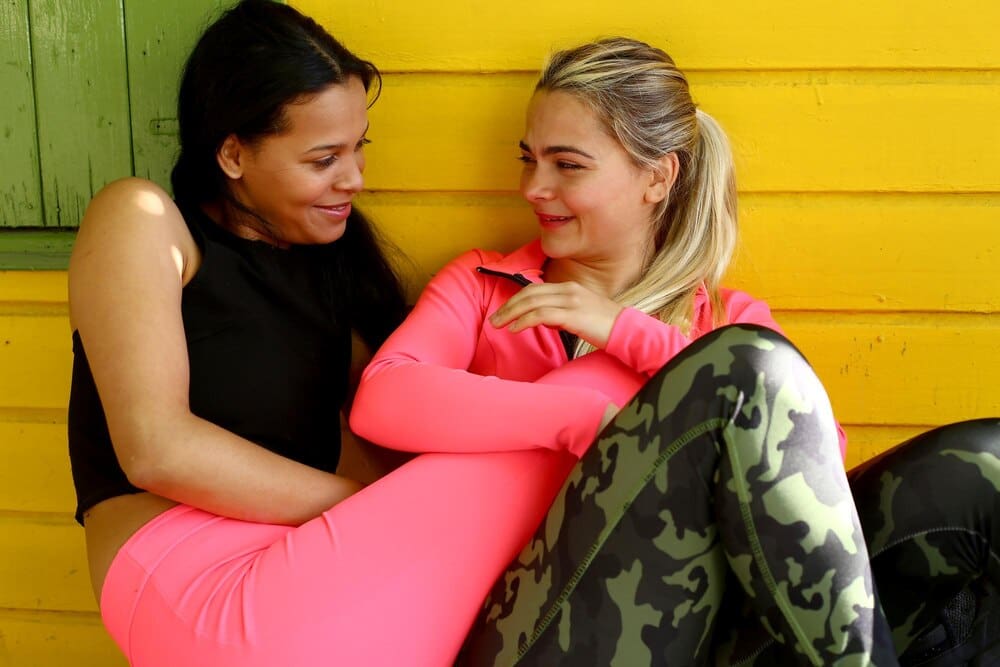 Two young, smiling women of the same race embrace, likely a couple, expressing affection.