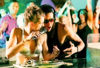 Two DJs stand side-by-side in a club, operating turntables.