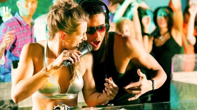 Two DJs stand side-by-side in a club, operating turntables.