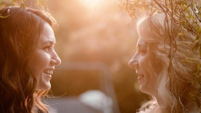 Two women with long hair are in a close-up portrait, facing each other at sunset.