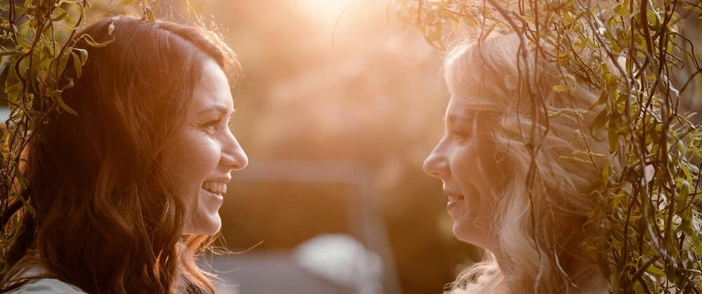 Two women with long hair are in a close-up portrait, facing each other at sunset.