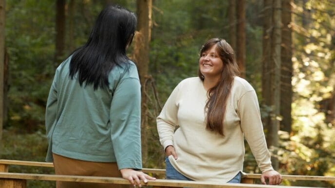 Two young friends converse while walking in a forest.