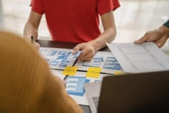 UI designer and customer collaborating, brainstorming mobile app interface wireframe designs, with color codes and a brief, in an office setting.