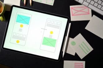 A person works at a desk with a laptop displaying a website template, surrounded by design tools.