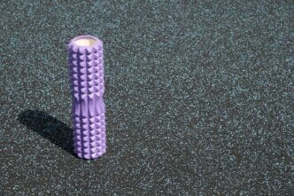 A purple foam roller rests on the grass, ready for an outdoor Pilates workout.