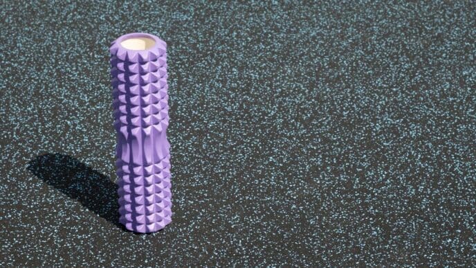 A purple foam roller rests on the grass, ready for an outdoor Pilates workout.