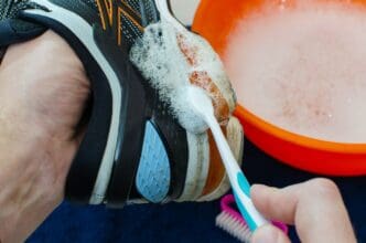 A person scrubs the sole of a dirty running shoe with a brush.