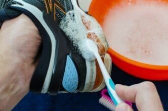 A person scrubs the sole of a dirty running shoe with a brush.